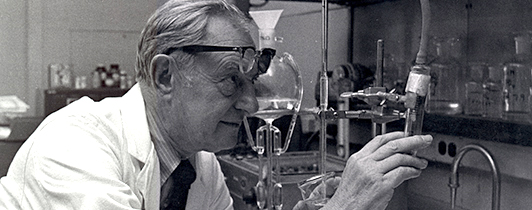 A man in a lab coat looks through an instrument.
